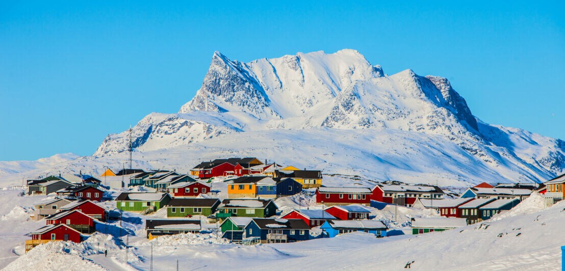 Schneebedeckte Landschaft und farbige Häuser in Nuuk mit dem Breg Sermitsiaq im Hintergrund.