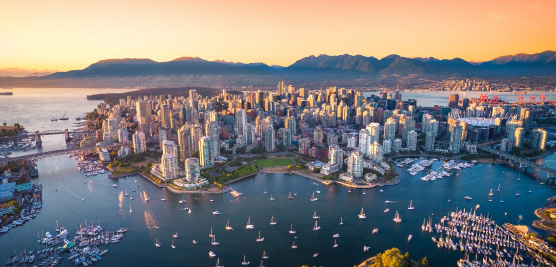 Luftaufnahme der Skyline von Vancouvers Innenstadt bei Sonnenuntergang mit vielen Booten im umliegenden Wasser.