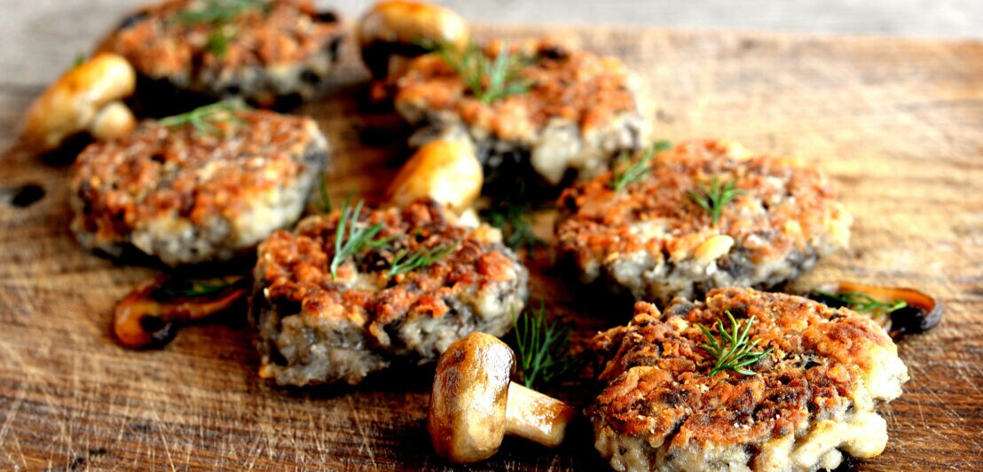 Gebratene Pilzschnitzel, angerichtet Kräutern und Pilzen auf einem Brett.