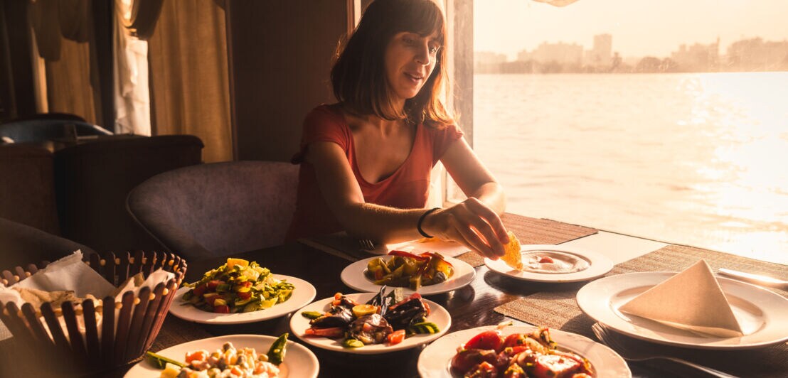 Eine Frau an einem Tisch dippt Brot in ein Gericht auf einem von mehreren Tellern.