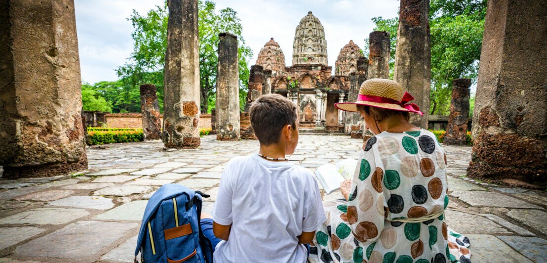 Eine Frau sitzt mit einem Jungen auf Steinen mitten in der thailändischen Tempelanlage Wat Mahathat.