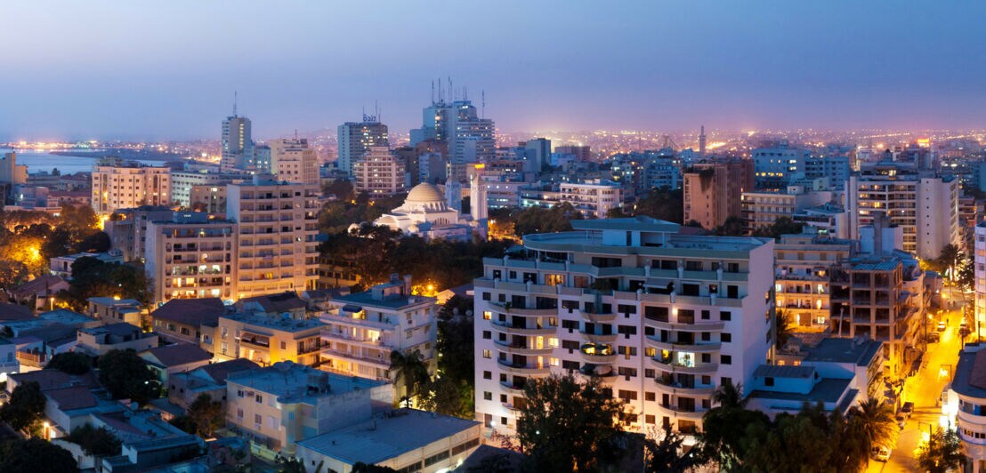 Erleuchtete Skyline von Dakar mit Hochhäusern und Moschee bei Nacht.