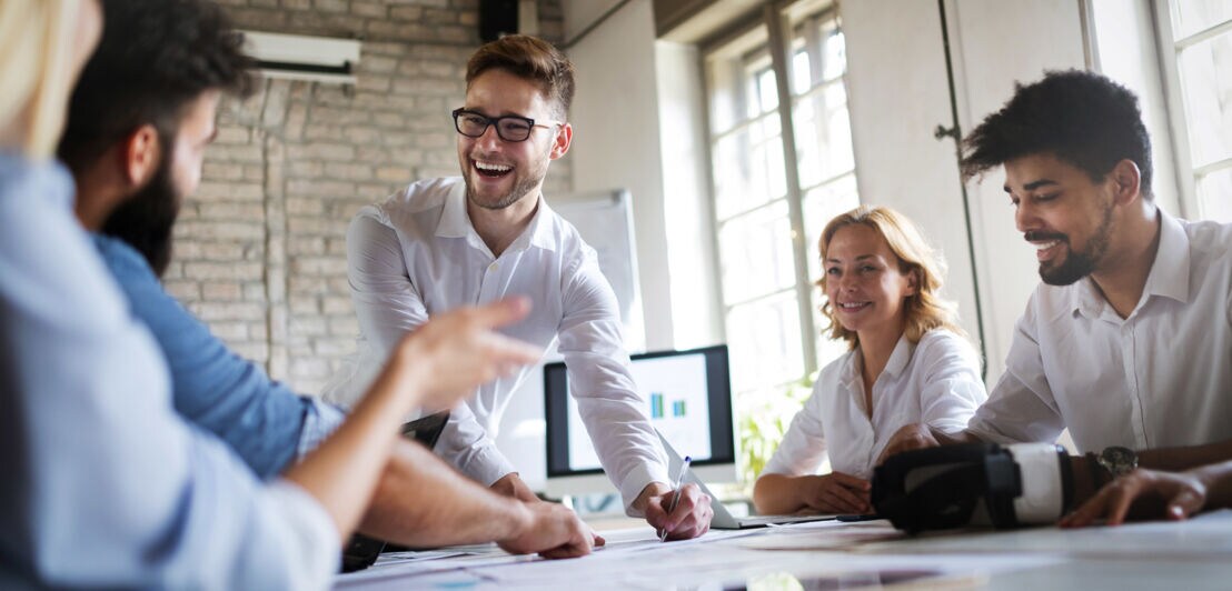 Fünf Personen agieren während eines Meetings mit Unterlagen auf einem Konferenztisch in einem hellen Büro.