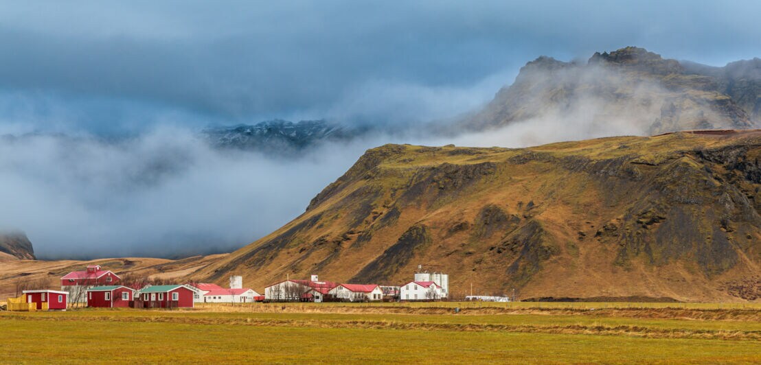 Faszinierende und neblige Herbstlandschaft rund um den Vulkan Eyjafjallajökull mit einer kleinen Siedlung im Vordergrund.