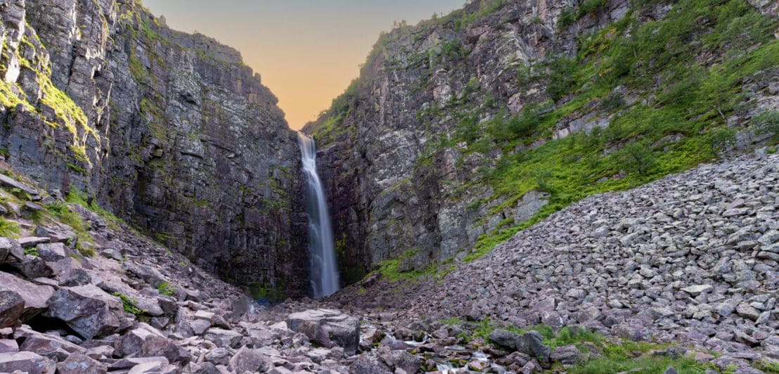 Hoher Wasserfall, der in einer Schlucht über eine steile Felswand in ein Felsbett stürzt.