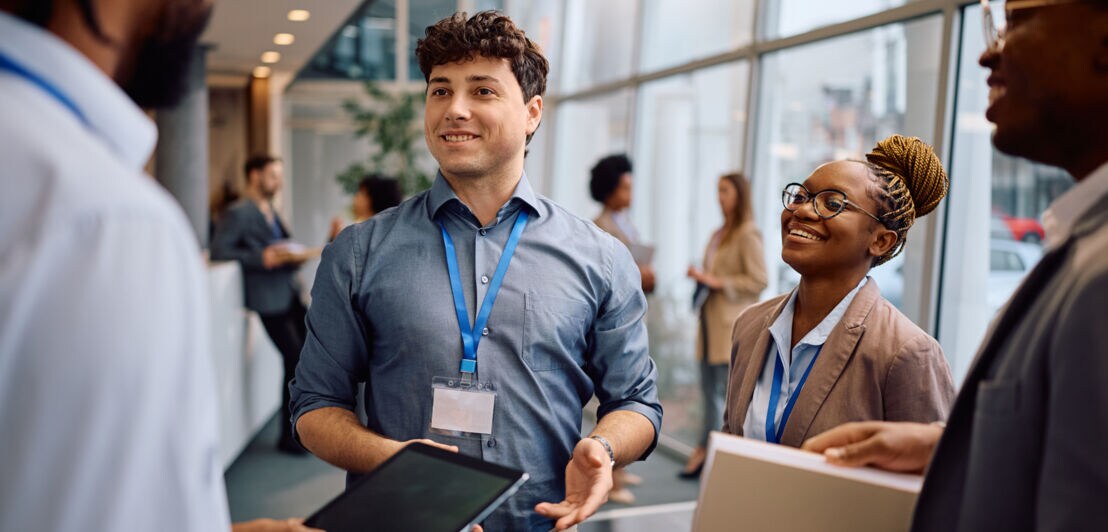 Mehrere Personen in legerer Business-Kleidung mit Konferenz-Lanyards stehen beisammen in einem Foyer.