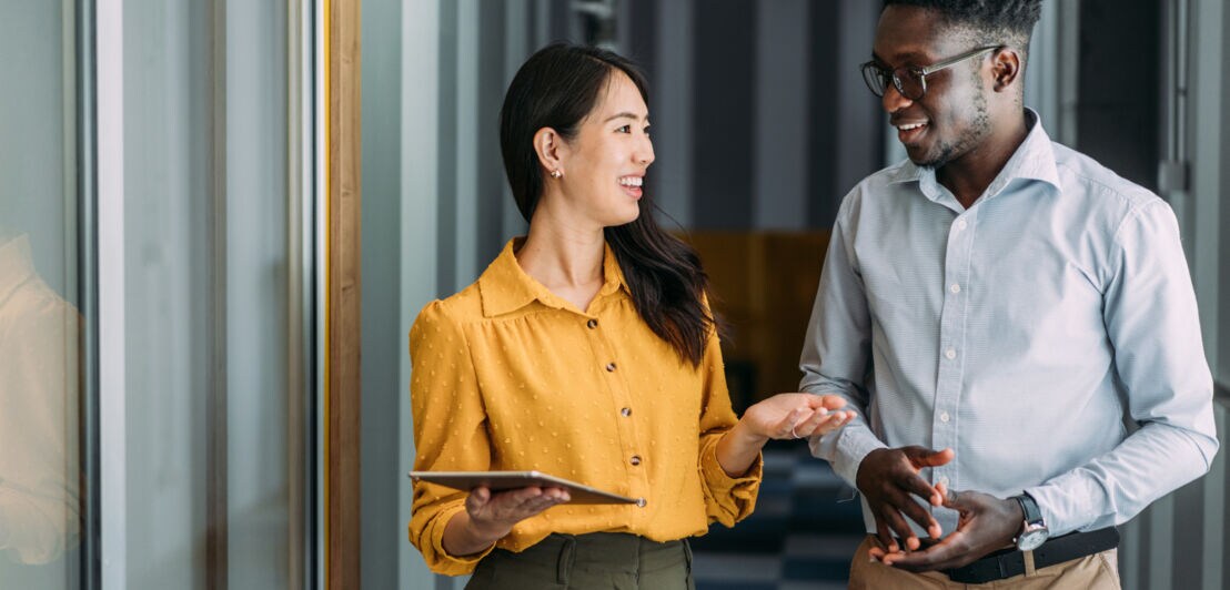 Eine Frau und ein Mann in Business-Kleidung kommunizieren freundlich in einem Flur.