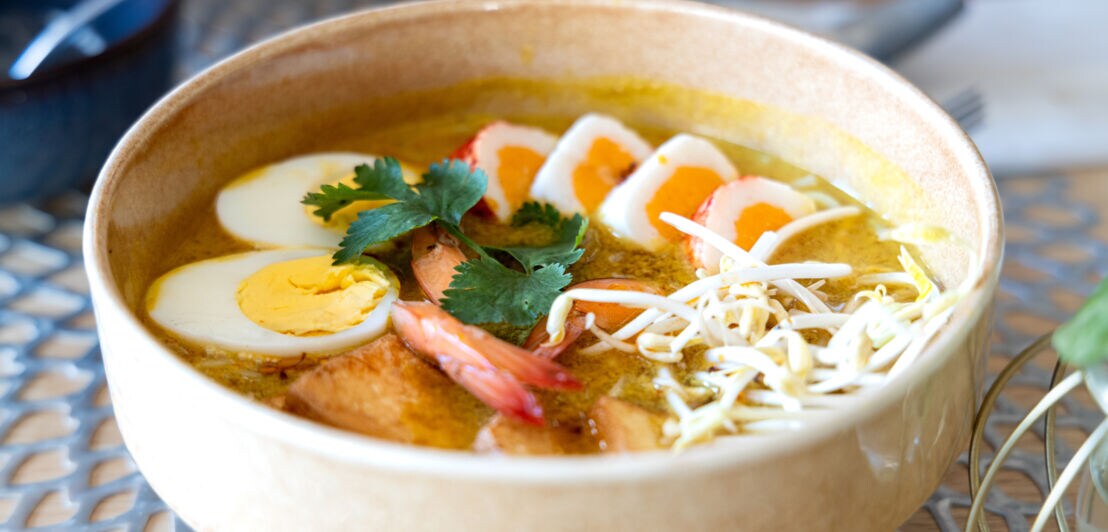 Schale mit Suppe, garniert mit gekochten Eihälften, Garnelen, Sprossen und Korianderblättern.