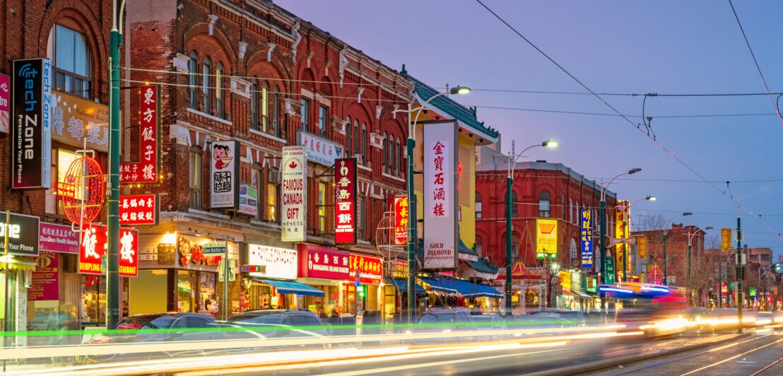 Straßenzug mit beleuchteten chinesischen Werbeschildern am Abend, im Vordergrund Lichtstrahlen von Autos durch Langzeitbelichtung.