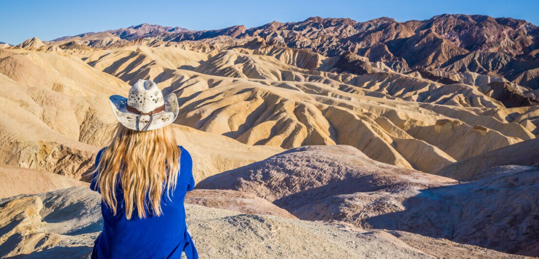 Eine Frau mit Sonnenhut schaut in die Wüstenlandschaft des Death Valley.