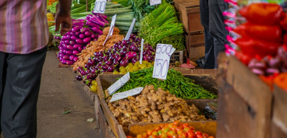 Holzboxen und Stapel mit Gemüse und Früchten sowie Preisschildern.
