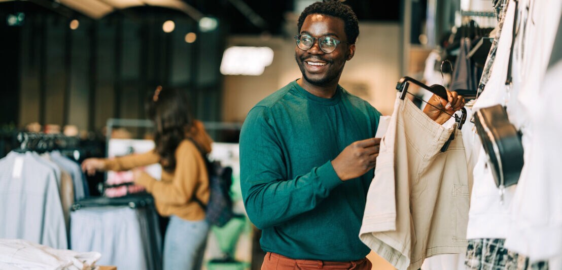 Ein lächelnder Mann hält eine kurze Hose an einem Bügel in seiner Hand in einem Modegeschäft.