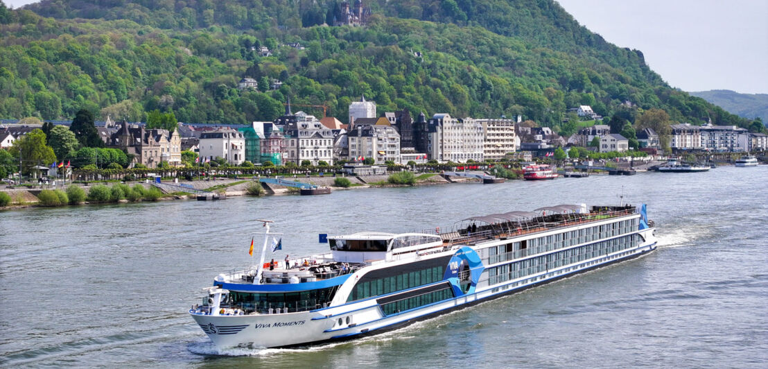 Flusskreuzfahrtschiff Viva Moments fährt vorbei an Kleinstadt am Ufer vor grüner Hügellandschaft mit Burg.