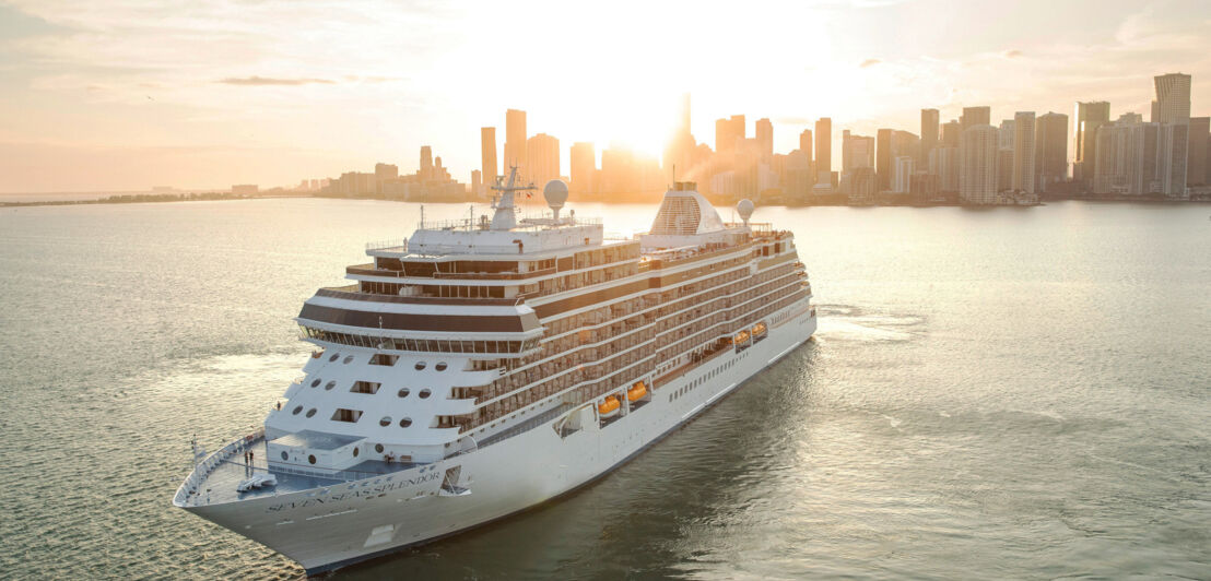 Kreuzfahrtschiff Seven Seas Splendor fährt vor der Skyline von Miami bei Sonnenuntergang.