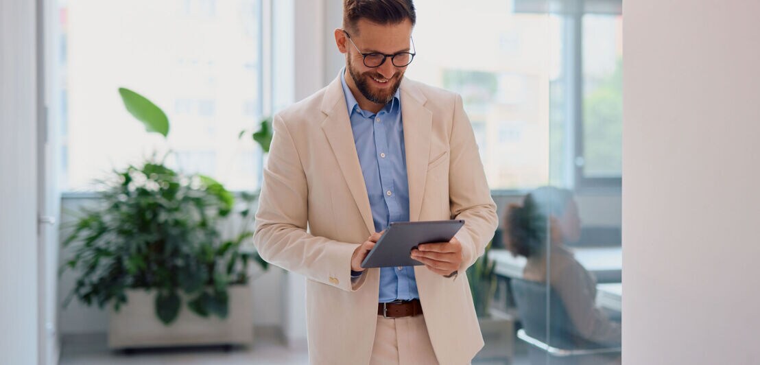 Ein gut gewählter Anzug gilt im Berufsleben als Symbol für Status und Seriosität.d und cremefarbenen Anzug bedient ein Tablet heller Büroumgebung.