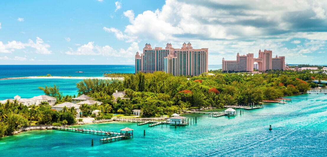 Hotelkomplex aus rosafarbenen Hochhäusern mit Türmen auf einer Insel mit tropischer Vegetation und Holzstegen im türkisblauen Meer.