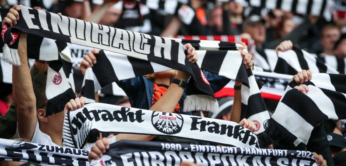 Zahlreiche hochgehaltene schwarz-weiße Schals mit „Eintracht Frankfurt“ Aufdruck in den Händen von Personen auf einer Tribüne.