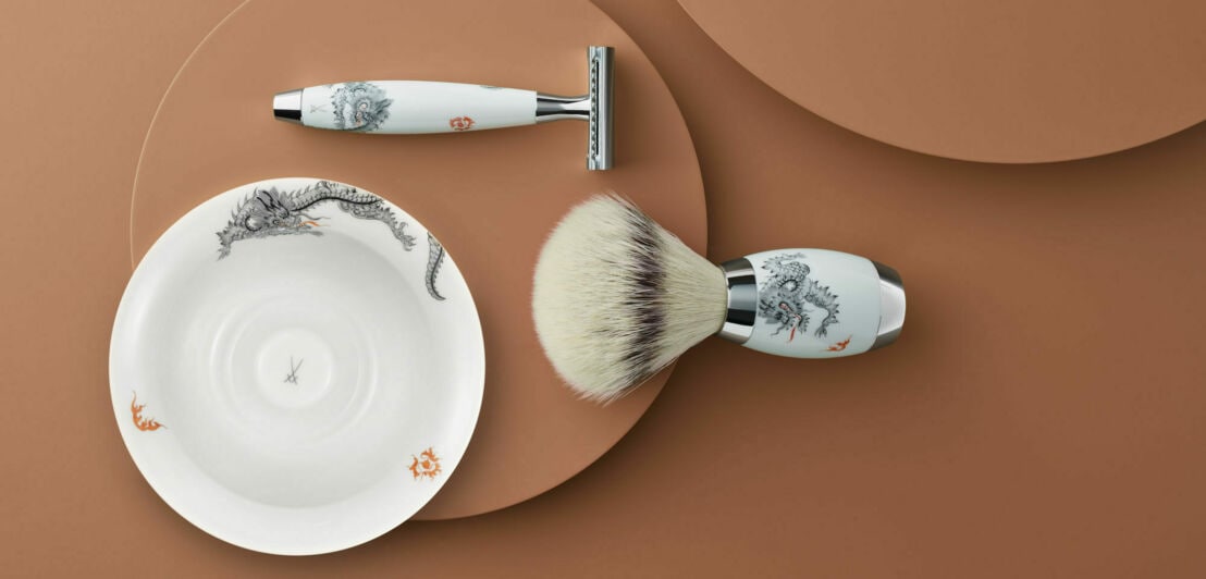 Handbemaltes Set aus Rasierer, Rasierpinsel und –schale auf mokkabraunem Untergrund.