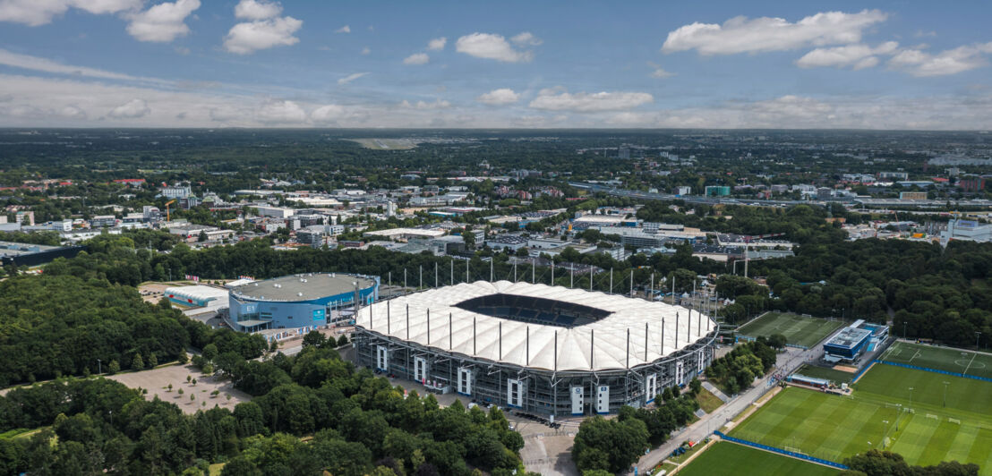 Fußballstadion mit weißem Dach in Grünanlage im städtischen Großraum von oben.