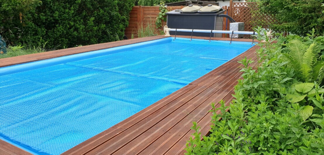 In einem Garten ist ein Pool mit einer blauen Plane bedeckt.