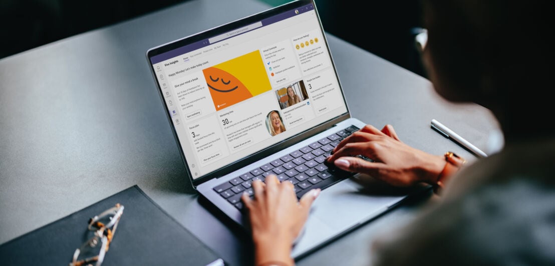 Eine Person an einem Schreibtisch sitzt an einem Laptop mit Microsoft-App auf dem Display.