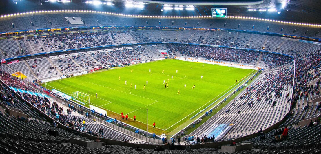 Blick auf ein Fußballfeld mit Spielern von der Tribüne im Inneren eines Fußballstadions.