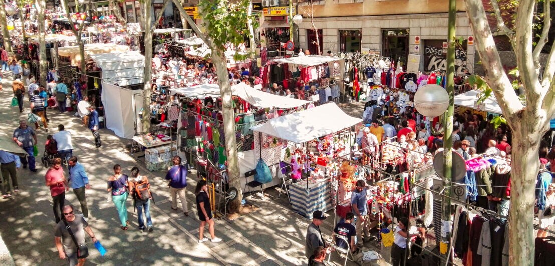 Zahlreiche Personen zwischen Flohmarktständen in einer Straße mit Platanen.