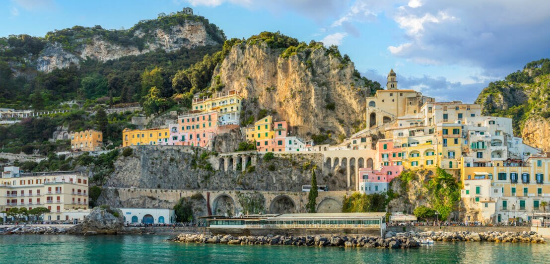 Ort mit bunten Häusern an der Amalfiküste, im Vordergrund türkisfarbenes Wasser.