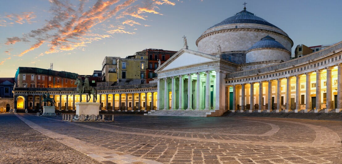 Die Piazza del Plebiscito in Neapel abends mit beleuchteten Kolonnaden.