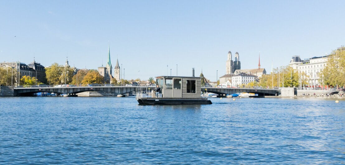 Eine Saunaboot auf einem See vor Stadtpanorama Zürichs.