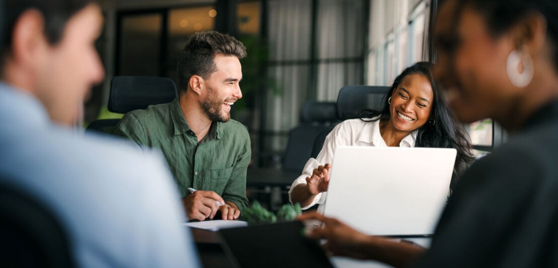 Vier Personen sitzen lächelnd beisammen an einem Arbeitstisch.