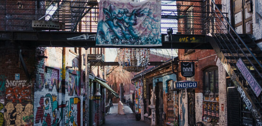 In einer Straße sind Wände und Mauern der Gebäude mit Graffitis bemalt.