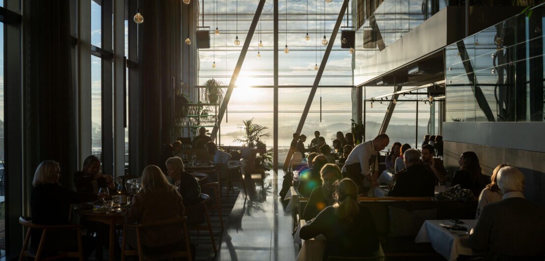 In einem Restaurant mit großen Glasfenstern stehen Tische und Stühle.