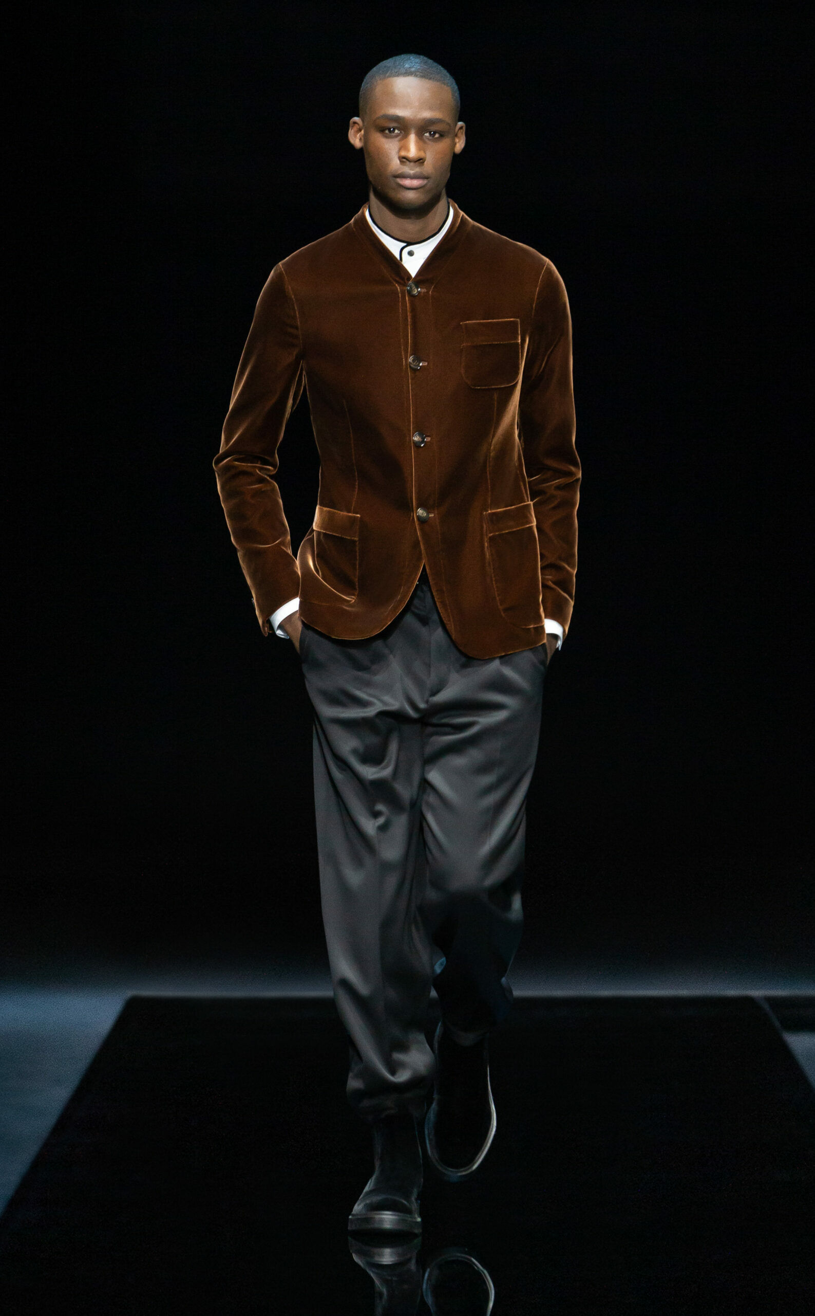 Ein Model auf dem Laufsteg, er trägt einen Samt-Sakko zu einer dunklen Stoffhose.