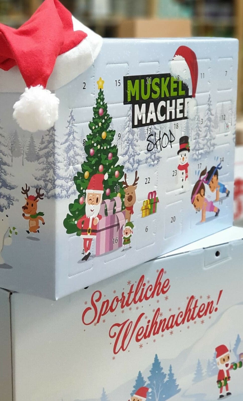 Zwei übereinander gestapelte Adventskalender-Boxen mit weihnachtlichen Motiven, obendrauf liegt eine Nikolausmütze