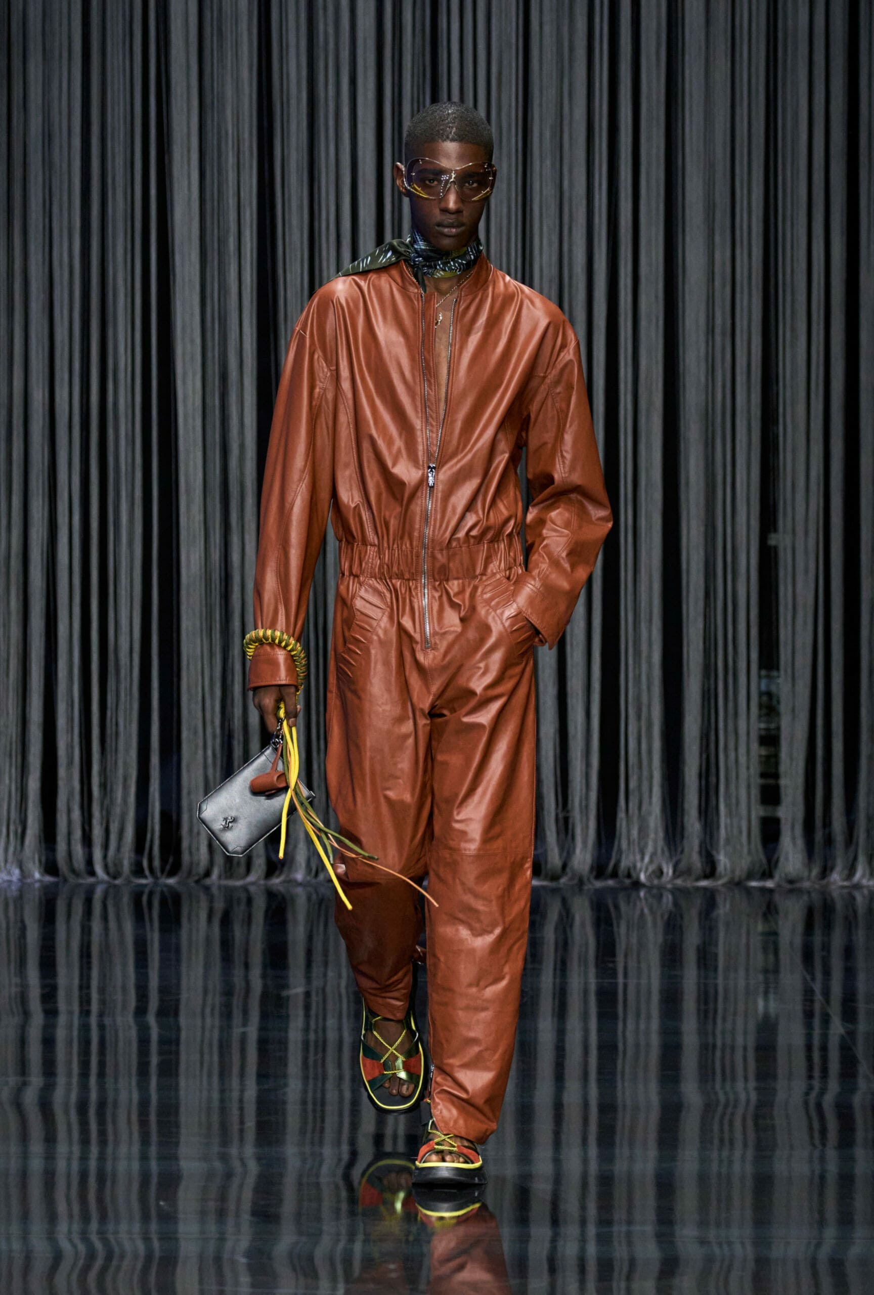 Ein männliches Model läuft in einem braunen Lederoverall über einen Laufsteg