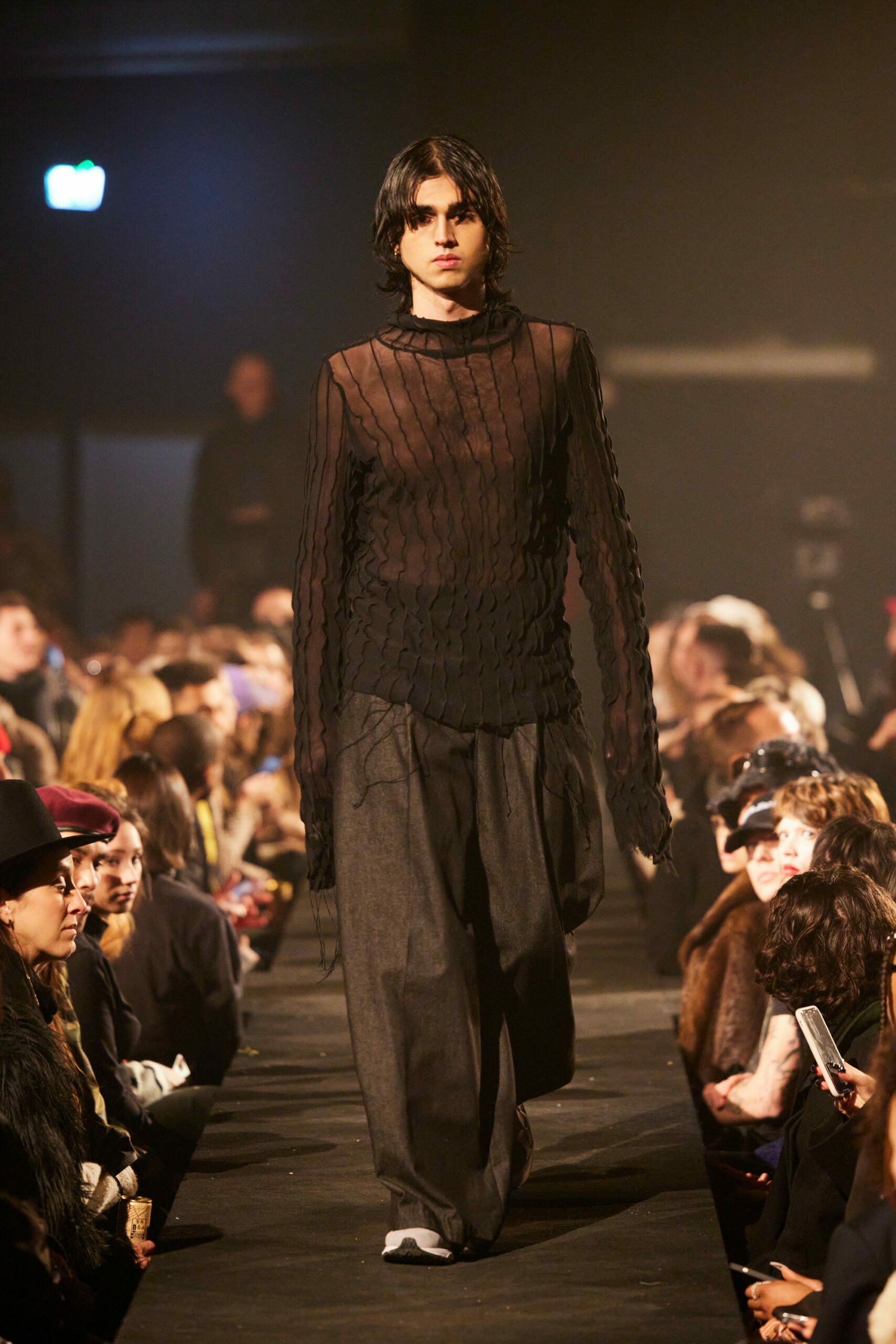 Ein männliches Model in schwarzem Look auf einem Catwalk