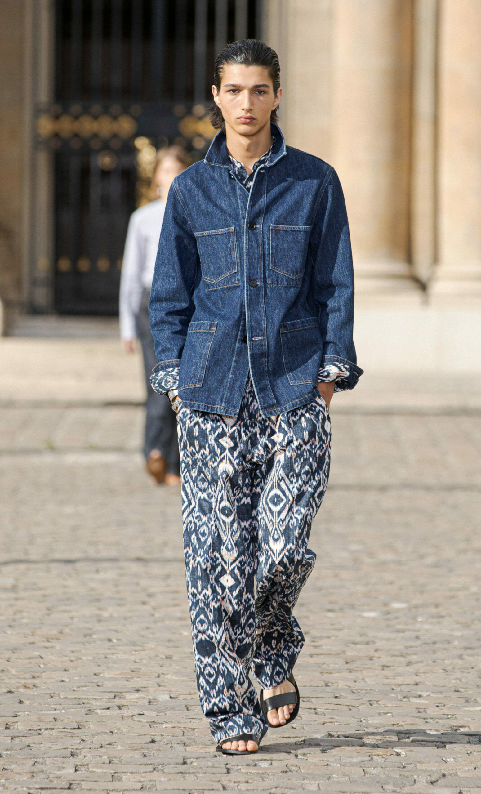 Männermodel in dunkelblauer Jeansjacke im Workwear-Style, dazu weite Hose mit blauem Ethnomuster