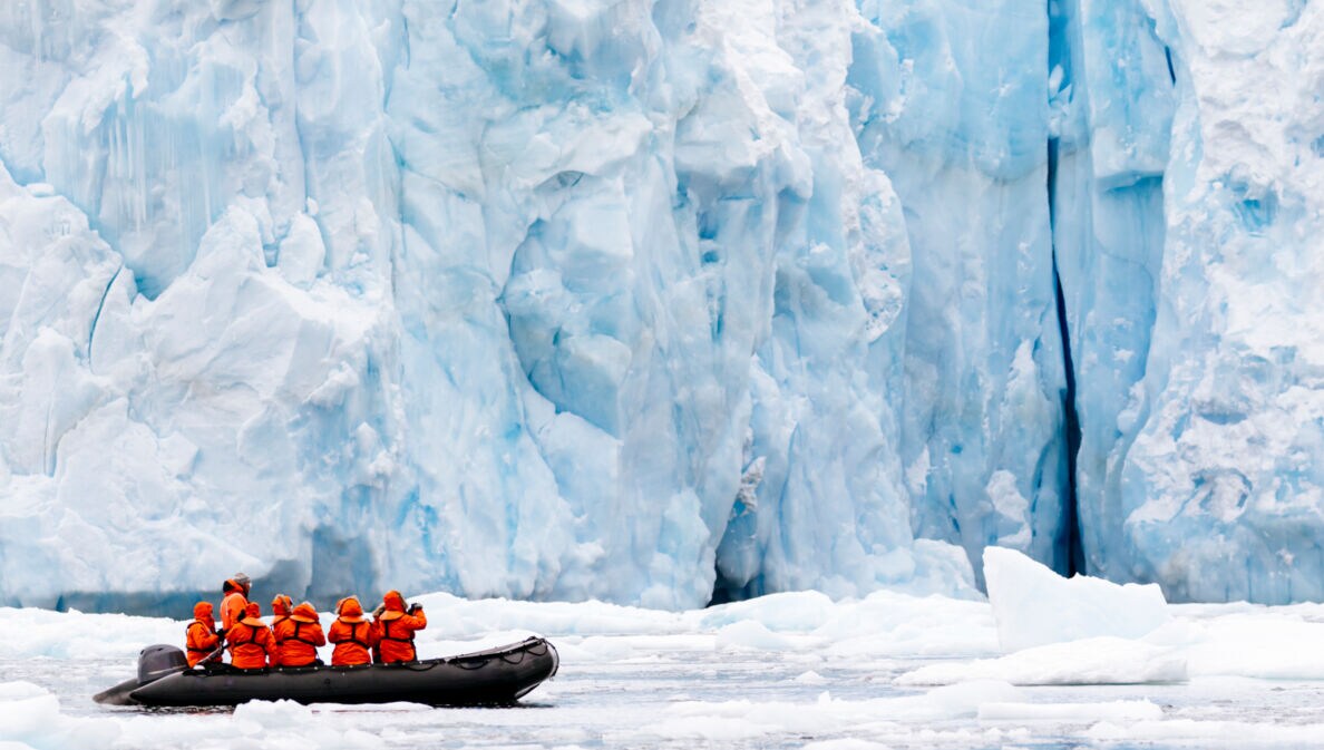 Ein Schlauchboot mit mehreren Personen vor einer gigantischen Eiswand
