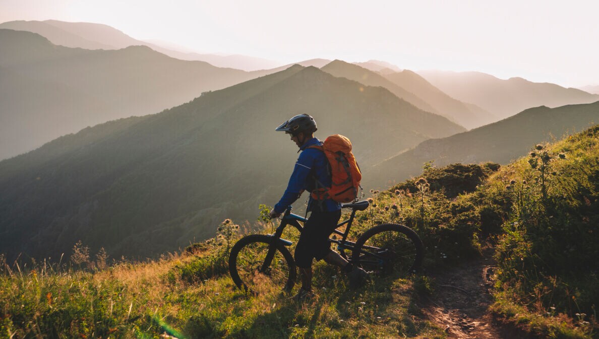 Mountainbiker steht mit seinem Rad auf einem Berg und schaut ins Tal