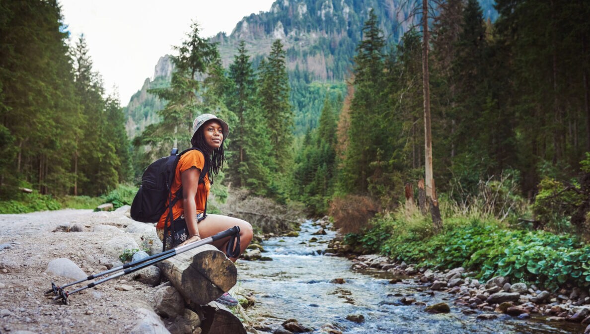Eine Frau sitzt mit Wanderausrüstung an einem Bach im Wald