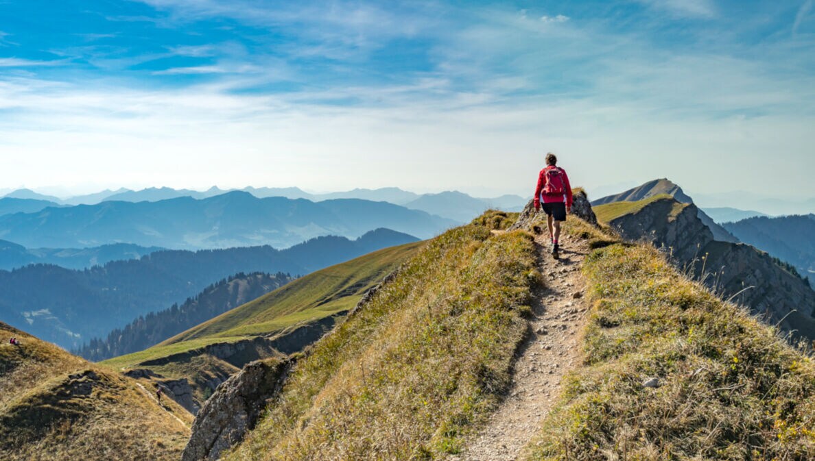 Rückansicht einer Person mit rotem Rucksack auf einem Wanderweg in den Bergen