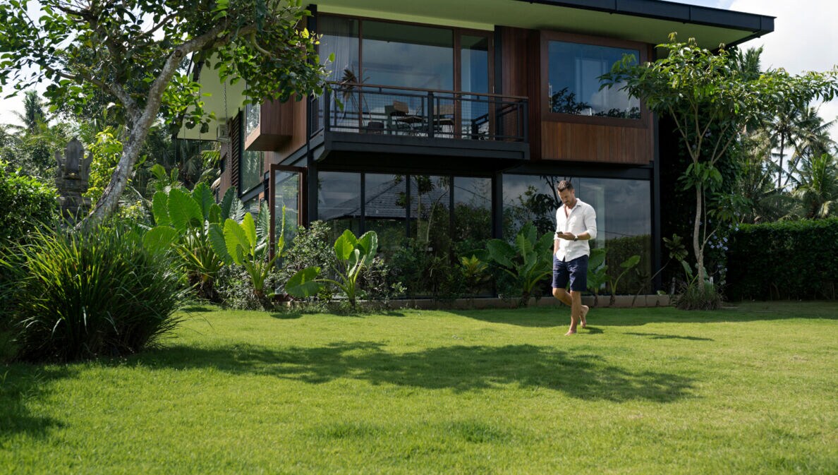 Ein Mann läuft mit Handy in der Hand über den Rasen hinter einem Haus