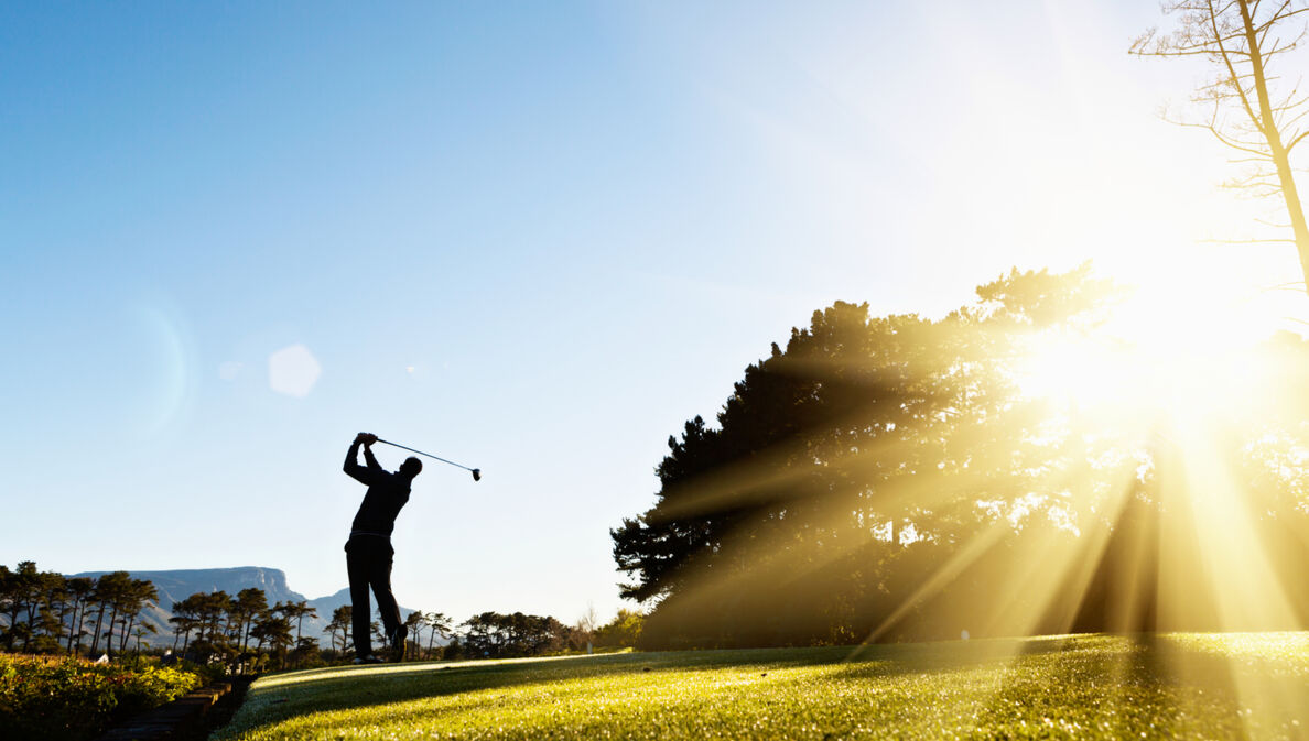 Die Silhouette eines ausholenden Golfspielers im Gegenlicht auf einem Golfplatz