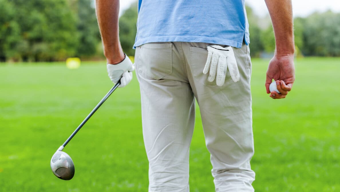 Rückansicht eines männlichen Golfspielers, der mit Golfball und Driver in der Hand weggeht