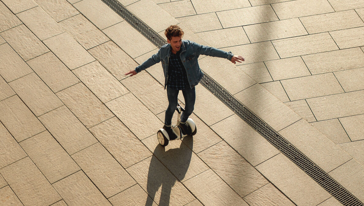 Ein lachender, junger Mann in Jeansjacke auf einem weißen Hoverboard
