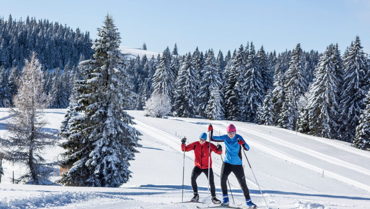 Zwei Skilanglaufende auf Loipe in hügeliger Winterlandschaft