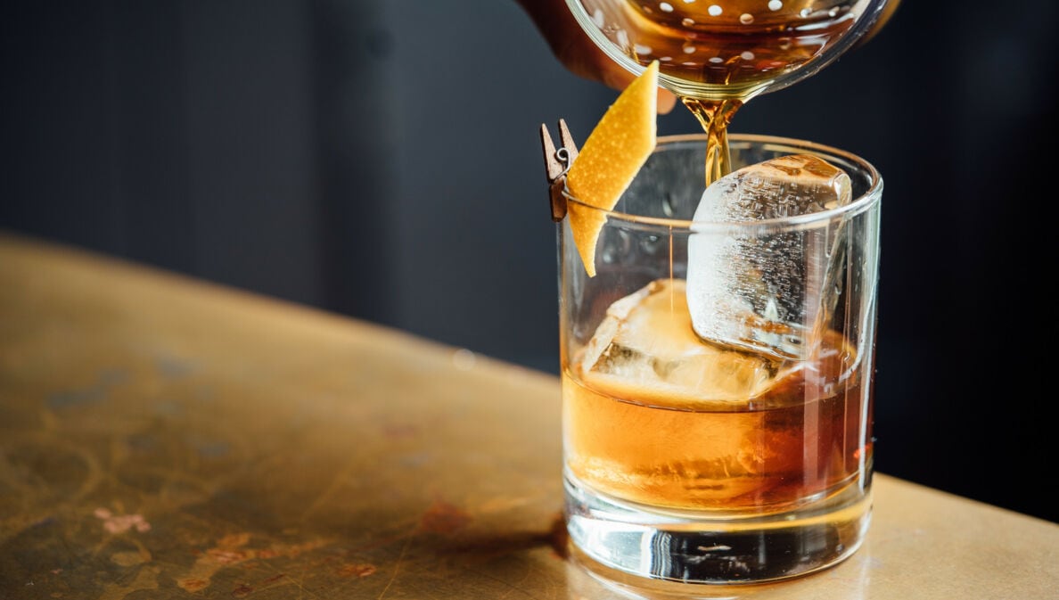 Ein Trinkglas mit Eis und Zitronenschale wird mit Whisky befüllt