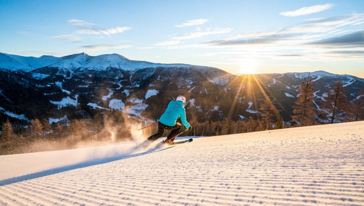 Eine Person auf Ski fährt bei Sonnenschein eine Piste hinab.