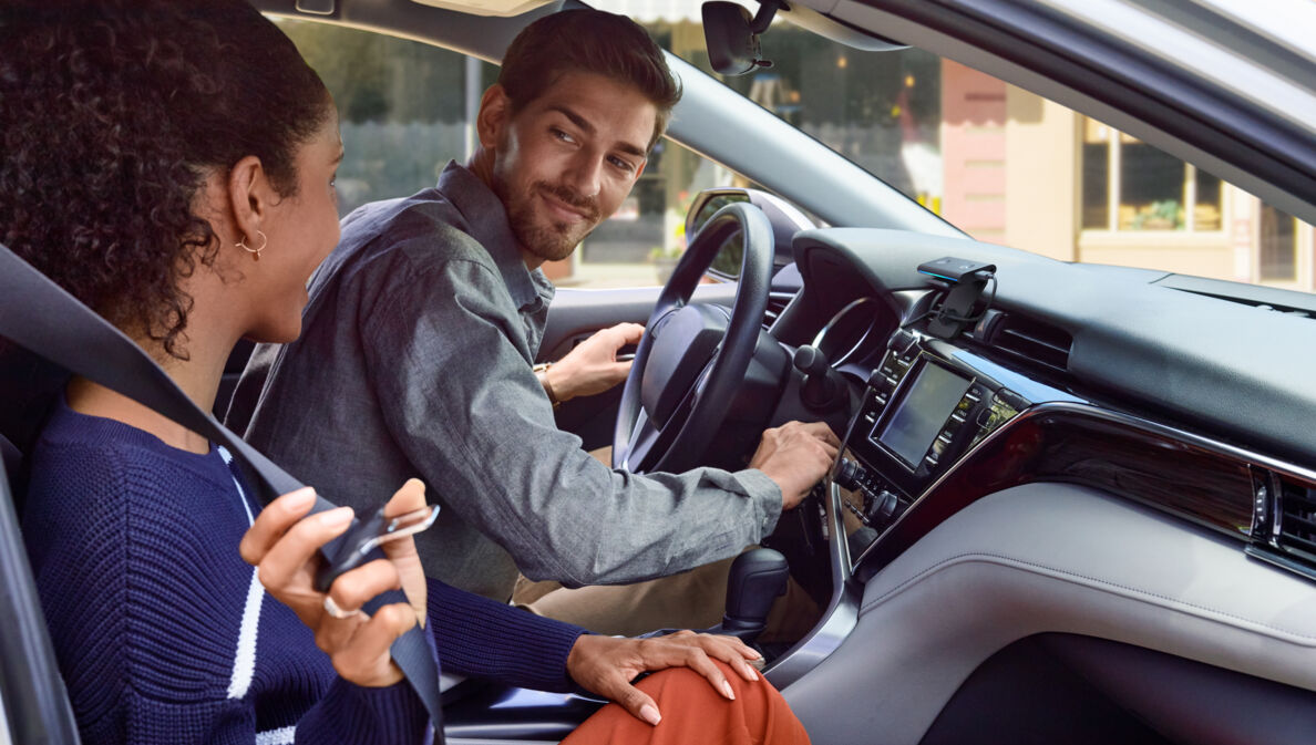 Ein junges Paar im Auto, auf dem Armaturenbrett ist Amazon Echo Auto verbaut.